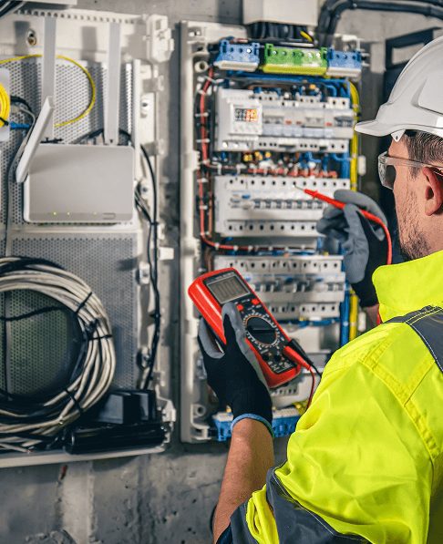 Electrician testing industrial electrical control panel with diagnostic equipment